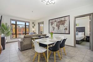 A modern living room with a dining area, a sofa, a coffee table, and a large window. - Resort Living Across from the Lake: Pool, Hot Tub, Gym & 3BR !! (Kelowna)