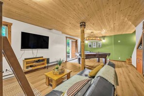 A living room with a wooden ceiling, a flat-screen TV, a pool table, and a sofa.