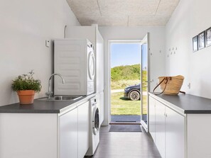 A compact kitchen with a washing machine, a sink, and a potted plant. - 5 Star Holiday Home in Glesborg (Glesborg)