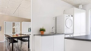 Una cocina moderna con armarios blancos, lavadora integrada y comedor con mesa y sillas de madera.