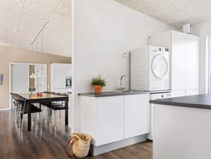 A modern kitchen with white cabinetry, a built-in washing machine, and a dining area with a wooden table and chairs. - 5 Star Holiday Home in Glesborg (Glesborg)