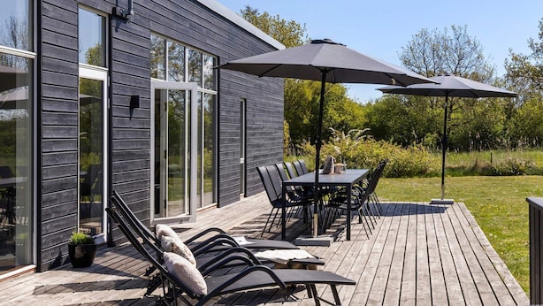 Un patio moderno al aire libre con terraza, una mesa de comedor y sillas, y dos sombrillas.