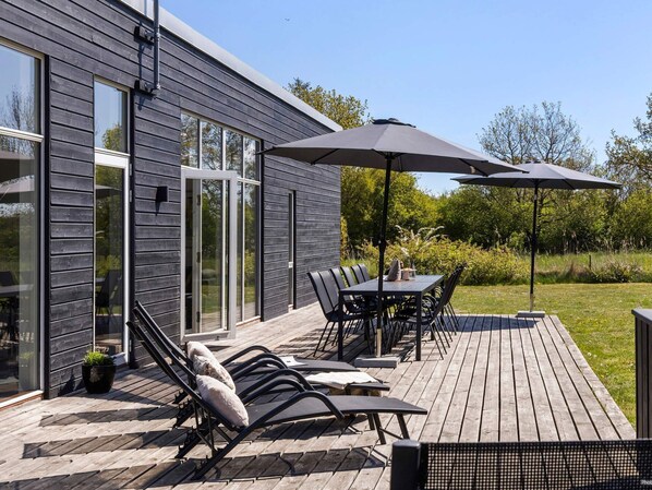 A modern outdoor patio with a deck, a dining table with chairs, and two umbrellas. - 5 Star Holiday Home in Glesborg (Glesborg)