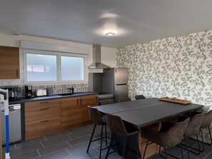 Une cuisine moderne avec des meubles en bois, un four encastré, un réfrigérateur et un coin repas comprenant une table et des chaises.