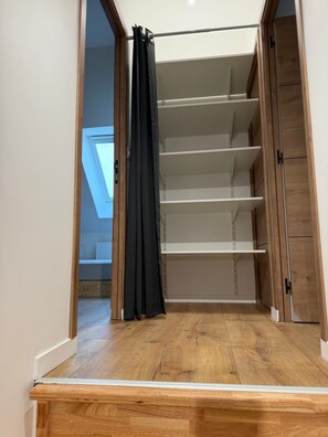 Una habitación con piso de madera, techo con tragaluz y armario con estantes.