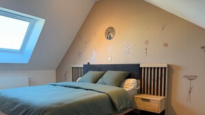Ein Schlafzimmer mit schrägem Dach, einem Oberlicht, einem Bett mit grüner Bettwäsche, einem Holz-Kopfteil und Wandstickern.
