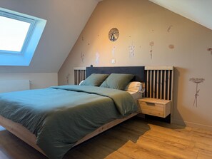 Een slaapkamer met een schuine kap, dakraam, een bed met groene beddengoed, een houten hoofdbord en muurstickers.
