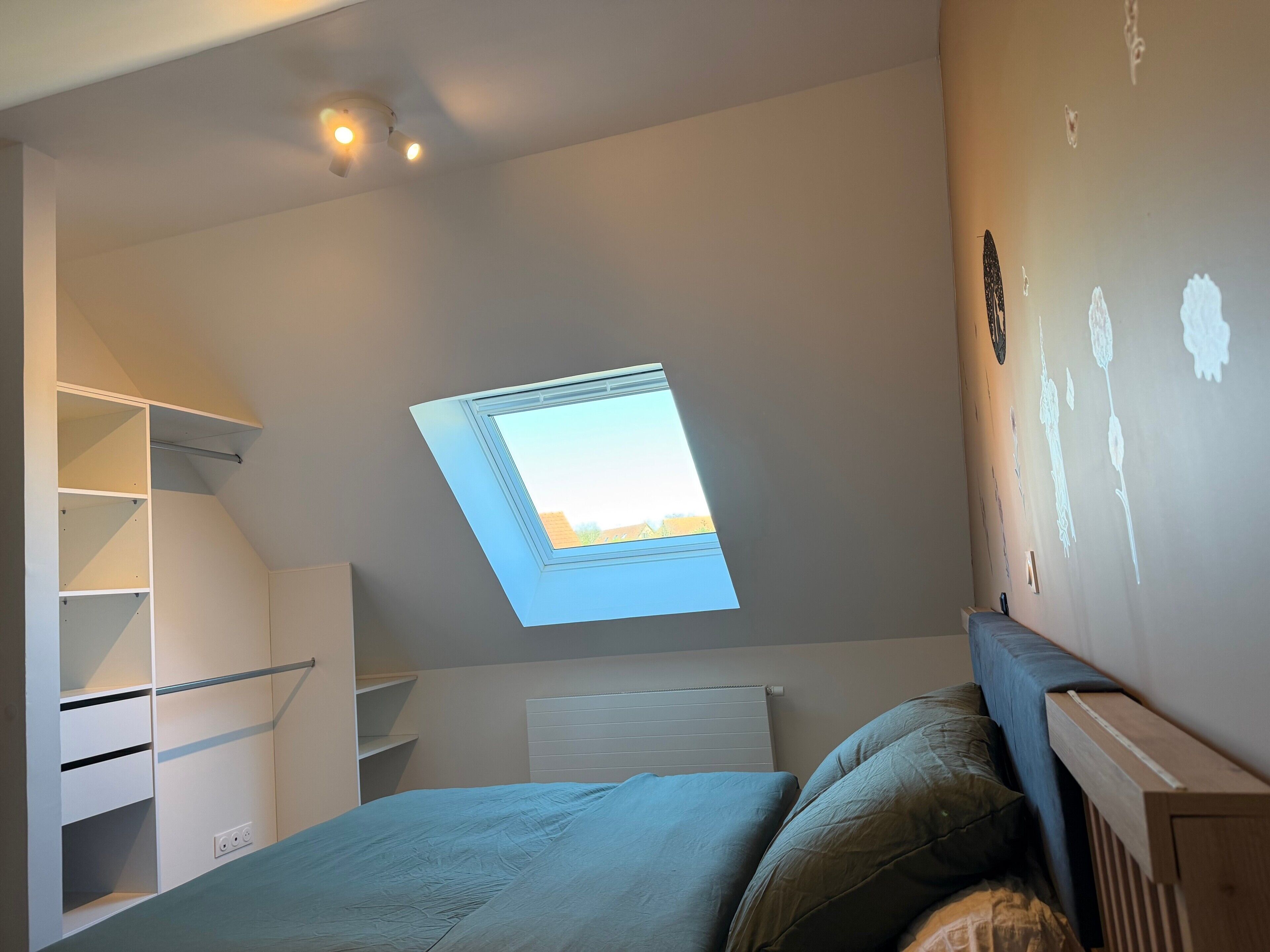 Una camera da letto con finestra sul tetto, un letto, un armadio e un termosifone.