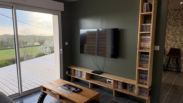 Ein Wohnzimmer mit Fernseher, Holzregalen mit Büchern, einem Couchtisch und Blick durch eine Schiebetür.