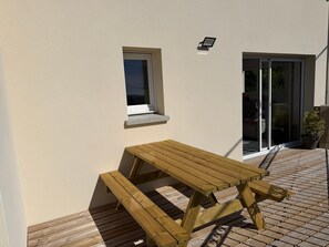 Une table de pique-nique en bois avec des bancs, une petite fenĂȘtre et un pot de fleurs sur une terrasse carrelĂ©e.
