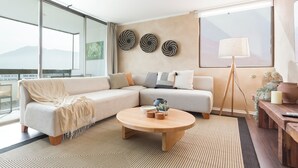 Een moderne woonkamer met een hoekbank, een ronde salontafel en een groot raam met uitzicht op bergen.