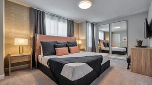 A modern hotel room with a large bed, bedside tables, a flat-screen TV, and a mirror. - 4BR Formosa Valley Home Near Disney (Kissimmee)