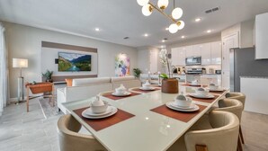 A modern dining area with a long table, chairs, and a chandelier. - 4BR Formosa Valley Home Near Disney (Kissimmee)