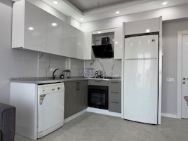 Una cocina moderna con armarios blancos, horno integrado y refrigerador.
