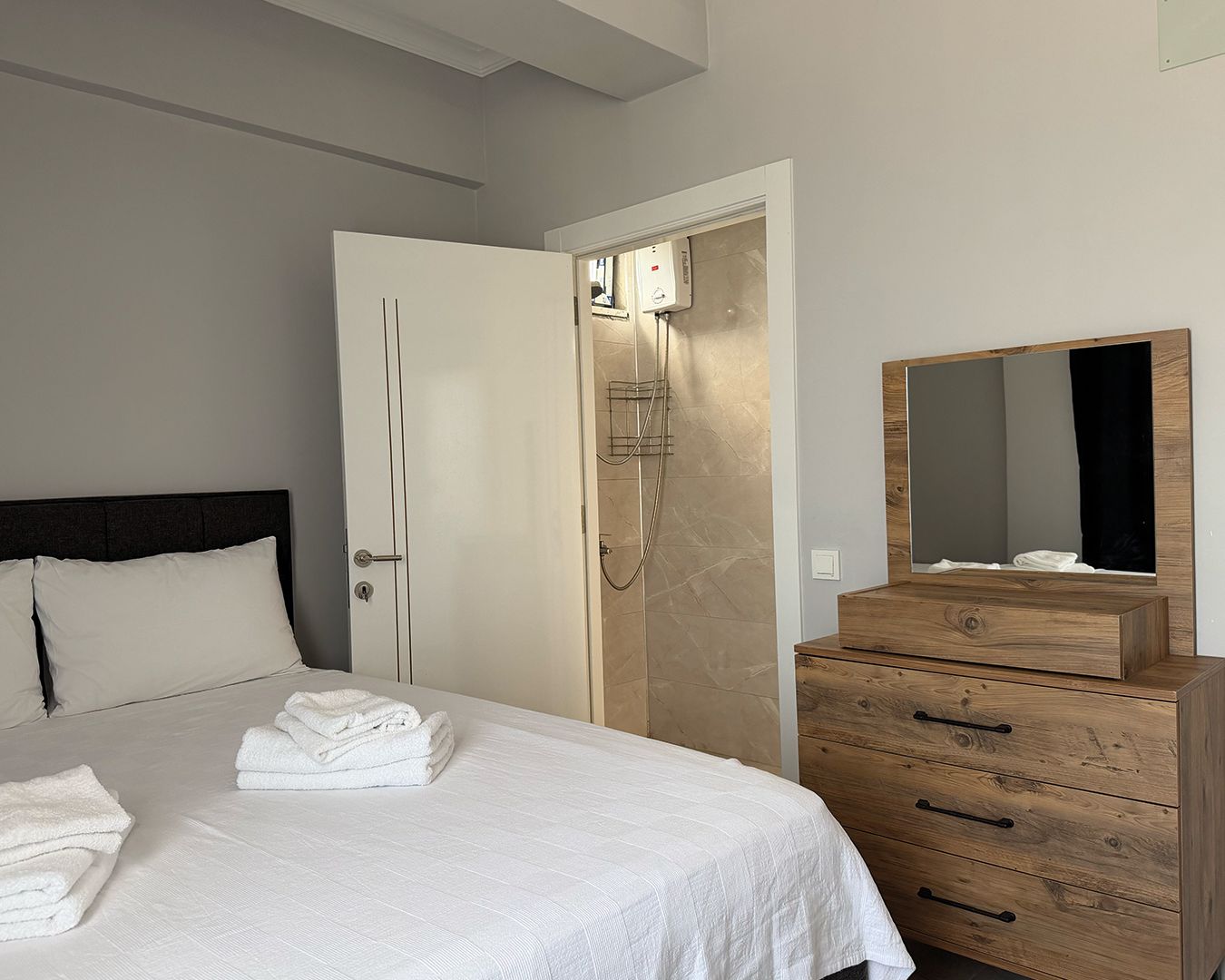 A bedroom with a bed, a wooden dresser, a mirror, and a shower.