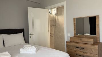 A bedroom with a bed, a wooden dresser, a mirror, and a shower.