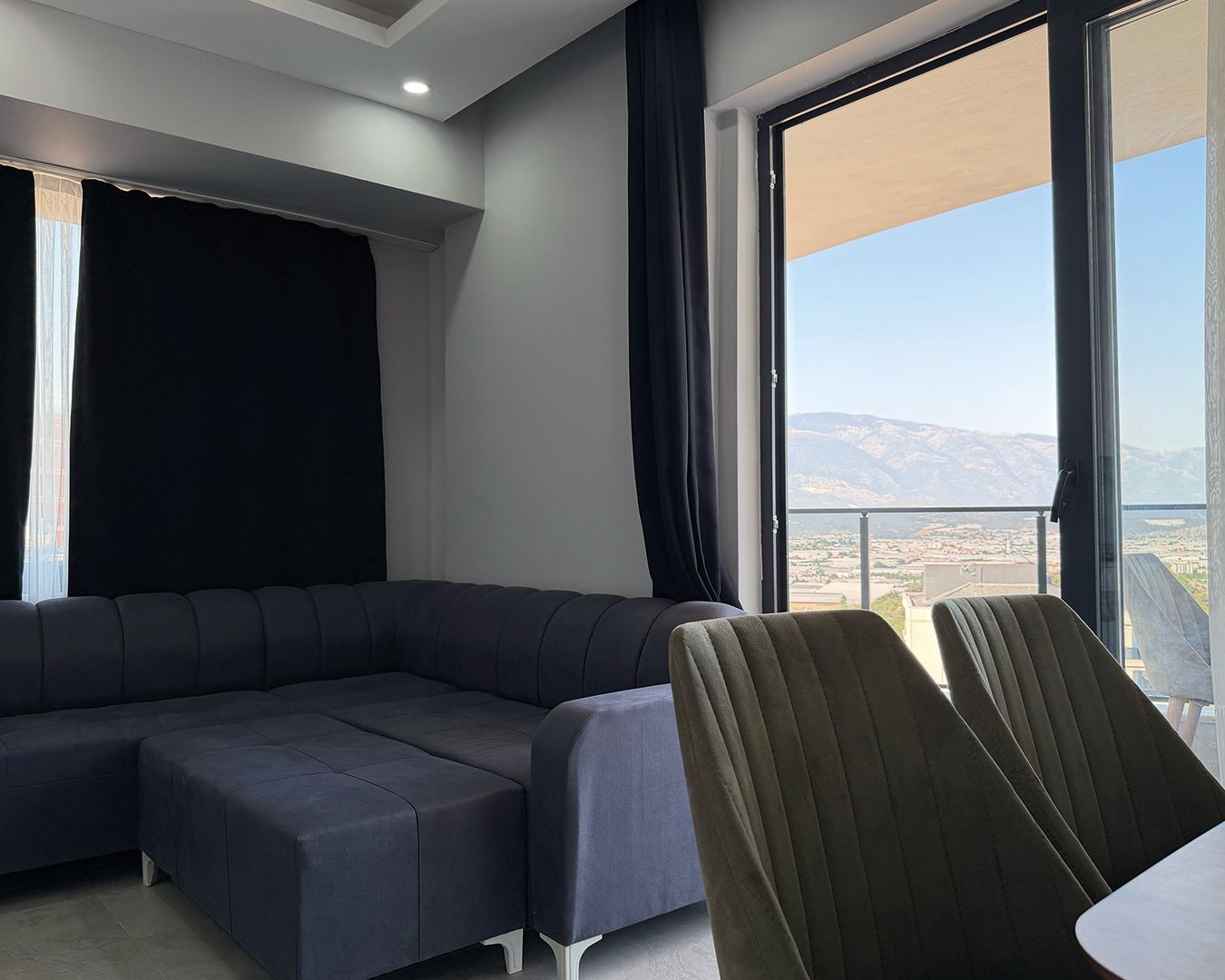 Ein modernes Wohnzimmer mit einer Eckcouch, einem Esstisch und einem großen Fenster mit Blick auf die Berge.