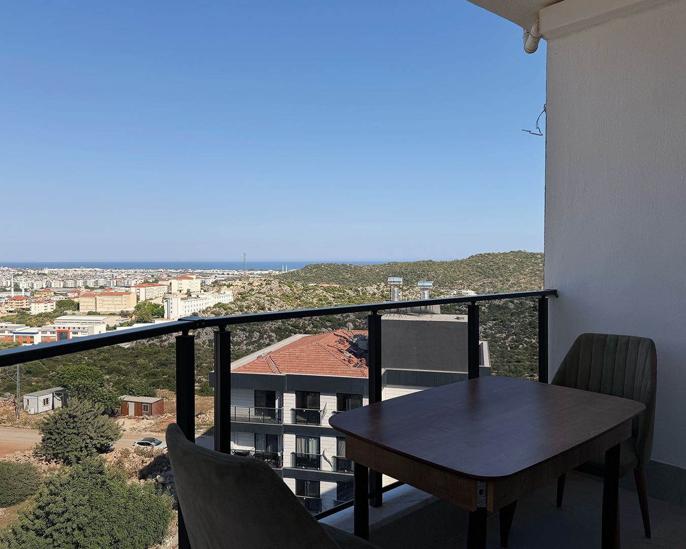 Ein Balkon mit Tisch und Stühlen, mit Blick auf eine Stadtlandschaft und eine hügelige Gegend.