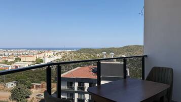 Ein Balkon mit Tisch und Stühlen, mit Blick auf eine Stadtlandschaft und eine hügelige Gegend.