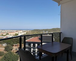 Varanda com mesa e cadeiras, com vista para o horizonte urbano e uma região montanhosa.