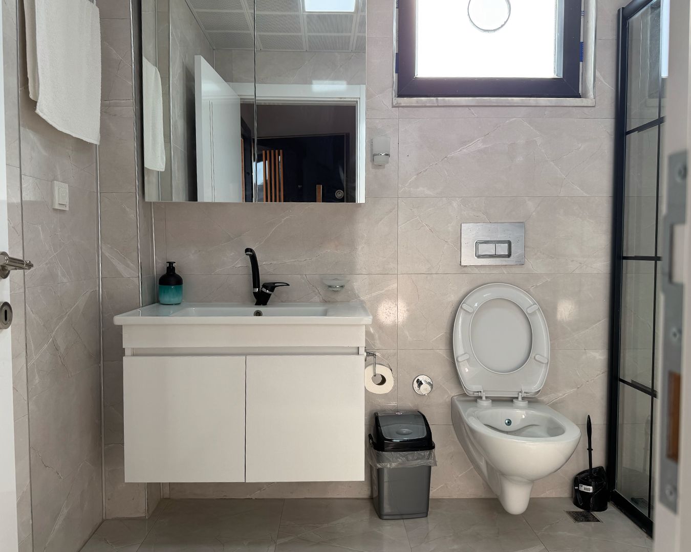 A bathroom with a white sink, a toilet, and a trash bin.