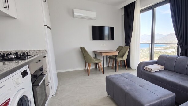 A modern living room with a grey sofa, a small table, and chairs. A washing machine is visible in the corner. - Doğuş Apart (Antalya)