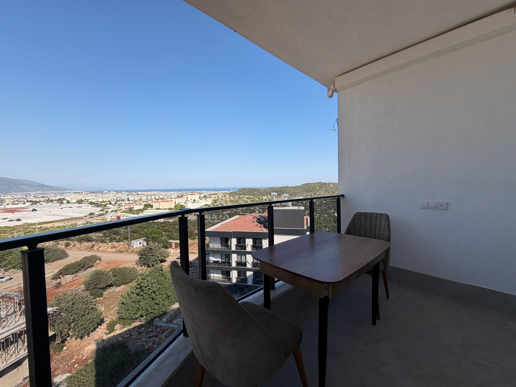 Ein Balkon mit Tisch und Stühlen mit Blick auf eine Stadtlandschaft und einen Hügel.