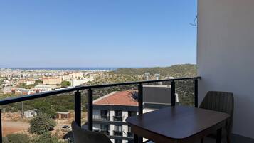 A balcony with a table and chairs, overlooking a cityscape and a hilly area.