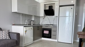 A modern kitchen with white cabinets, a black oven, and a refrigerator. - Doğuş Apart (Antalya)