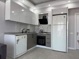 Una cocina moderna con armarios blancos, horno empotrado, lavavajillas y refrigerador.