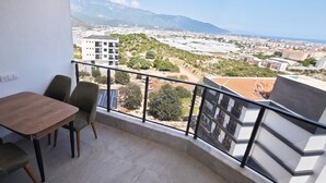 A balcony with a table and chairs, offering a view of a cityscape and mountains. - Doğuş Apart (Antalya)