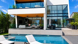 Ett modernt hus i två våningar med pool, utomhusmöbler och en balkong.