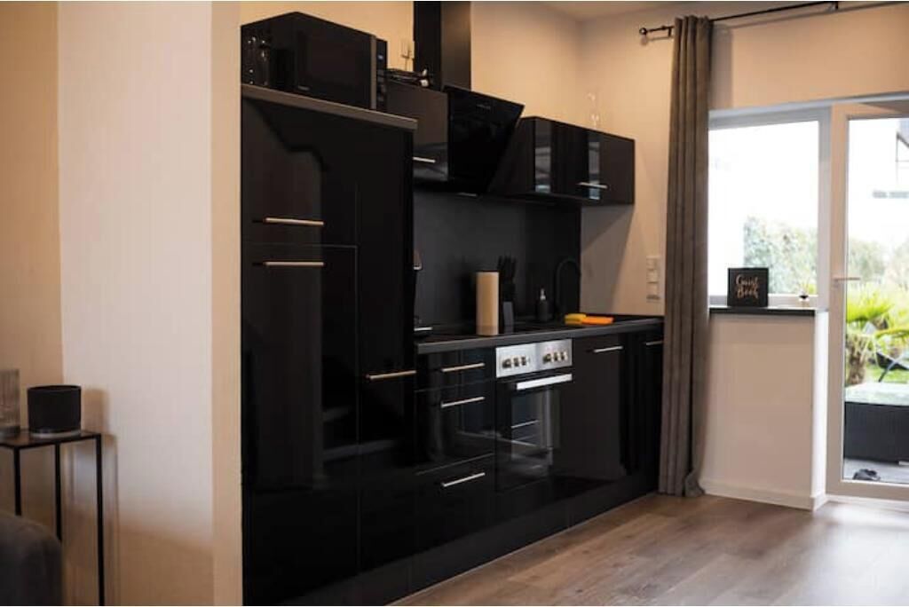 Une cuisine moderne avec des meubles de rangement noirs, un four encastré et une fenêtre avec des rideaux.