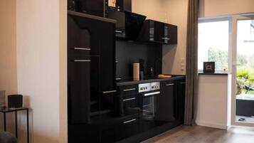 Une cuisine moderne avec des meubles de rangement noirs, un four encastré et une fenêtre avec des rideaux.