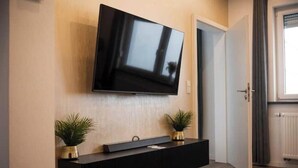 A flat-screen TV mounted on a wall above a black console with two potted plants. - Modern House KO26 (Koblenz)