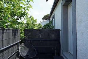 Un petit espace extérieur avec une chaise en métal, une clôture noire et un bâtiment blanc.