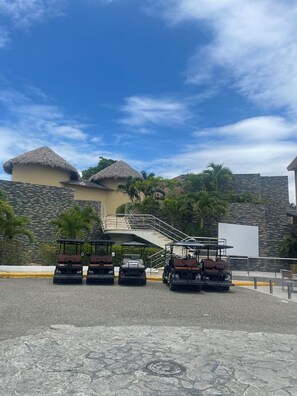 Ein Resort mit strohgedeckten Gebäuden, einer gepflasterten Fläche mit Golfcarts und einer Treppe, die zu einer höheren Ebene führt.