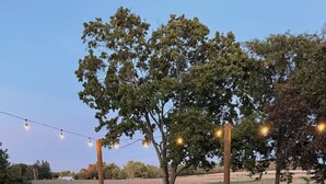Un área de estar al aire libre con sillas tipo Adirondack y una mesa redonda, rodeada de grava y luces colgantes.