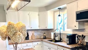Una cocina moderna con armarios blancos, una isla de madera, una estufa a gas y un lámpara colgante.