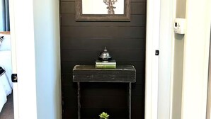 Un pasillo con paredes de madera oscura, un cuadro con la imagen de un molino, una pequeña consola con una planta y una puerta a la derecha.
