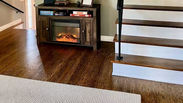 Una escalera con escalones de madera y barandilla negra, una chimenea con repisa, y un televisor de pantalla plana montado en la pared.