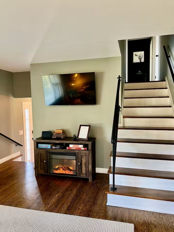 A staircase with wooden steps and a black railing, a fireplace with a mantel, and a flat-screen TV mounted on the wall.