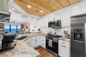 A modern kitchen with white cabinets, stainless steel appliances, a granite countertop, and a view of the ocean. - NEW | Beachfront Luxury · Beach Setup Included 🌊 (Panama City Beach)
