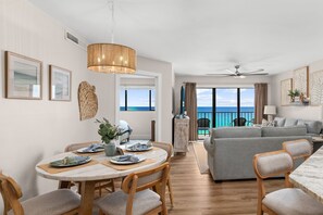 A modern living room with a dining area, a ceiling fan, and a view of the ocean. - NEW | Beachfront Luxury · Beach Setup Included 🌊 (Panama City Beach)