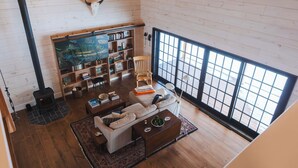 Un salon chaleureux avec une cheminée, des murs en bois, une grande fenêtre et une bibliothèque.
