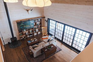 Ein gemütliches Wohnzimmer mit Kamin, Holzwänden, einem großen Fenster und einem Bücherregal.