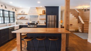 Une cuisine moderne dotée d’un îlot central, de tabourets de bar, d’un réfrigérateur en acier inoxydable et d’un escalier en bois.