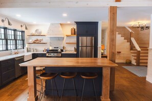 Eine moderne Küche mit einer zentralen Kochinsel, Barhocker, einem Edelstahlkühlschrank und einer Holztreppe.