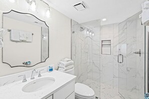A modern bathroom with a marble sink, a large mirror, a toilet, and a glass-enclosed shower area. - Sundunes 173 (Navarre)