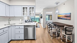 A modern kitchen with white cabinets, a central island, and a dining area with wooden tables and chairs. - Sundunes 173 (Navarre)